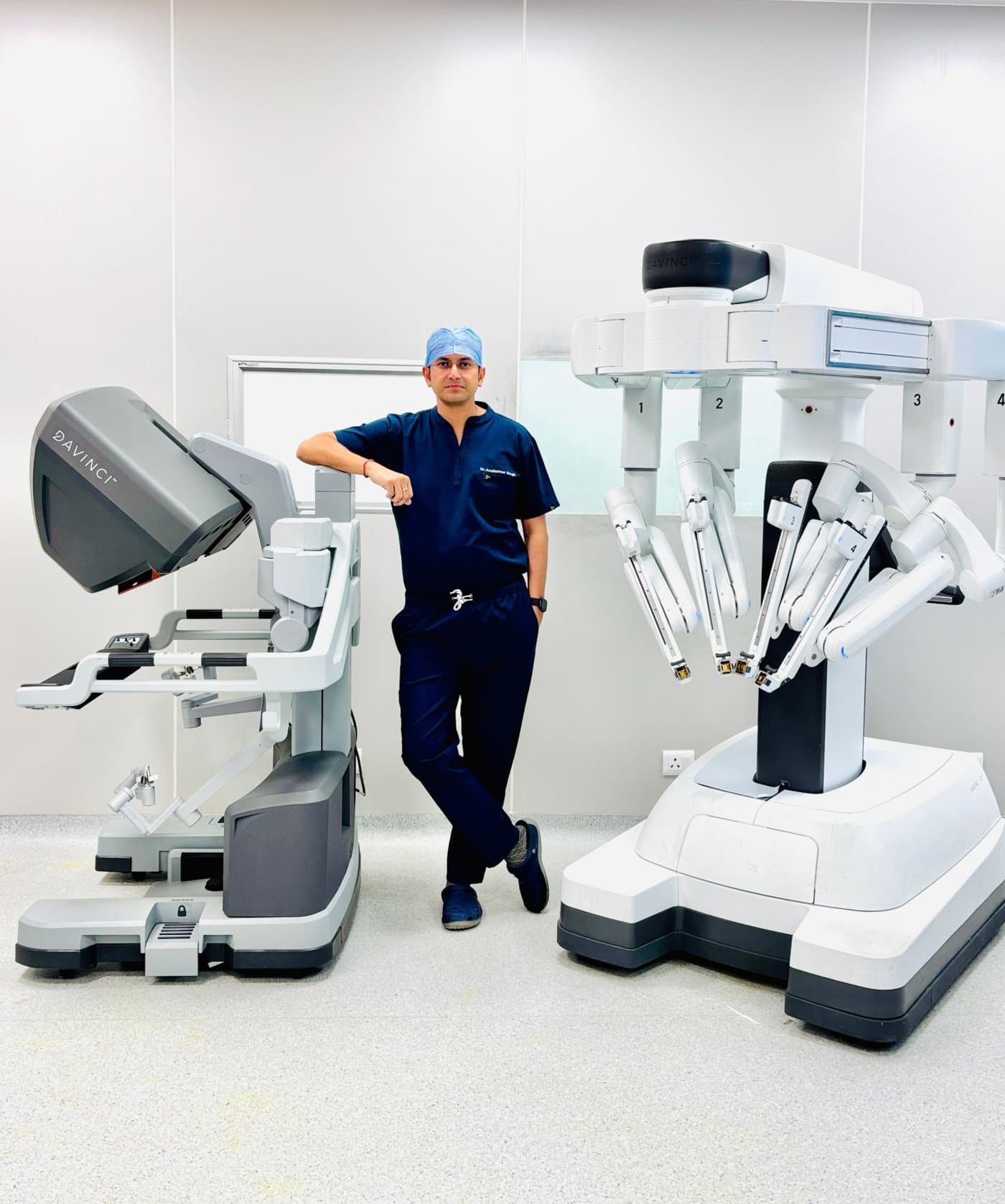 Dr. Anshuman Singh standing between the surgeon console and the patient-side unit of a robotic surgical system